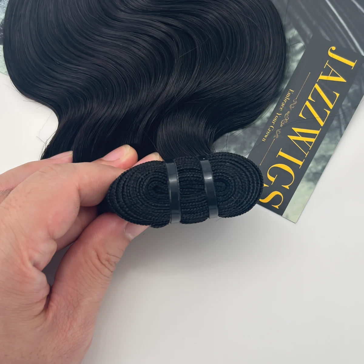 Hand holding the rolled weft of a JAZZWIGS Raw Vietnamese body wave hair bundle in natural black.