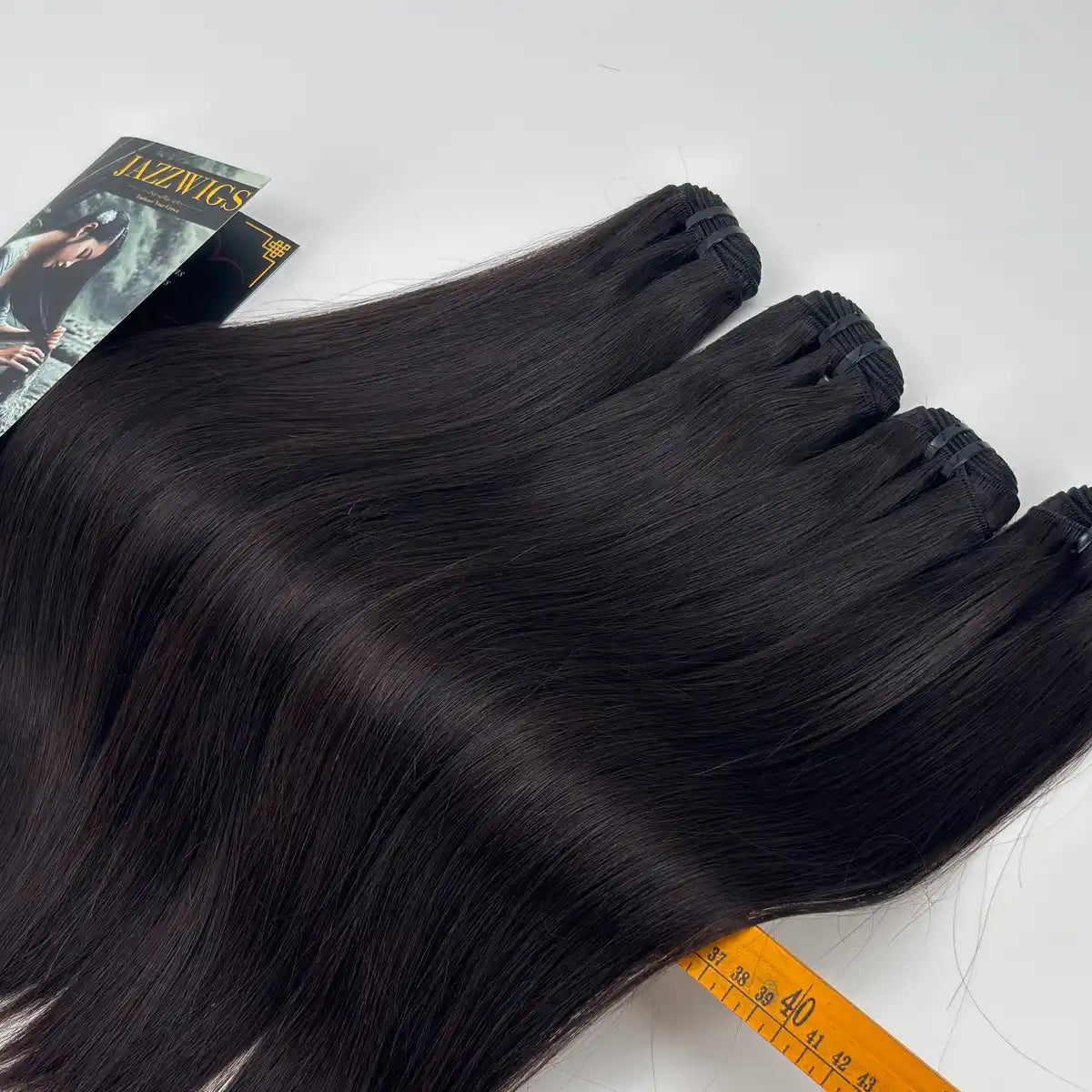 Close-up of JazzWigs Raw Vietnamese Straight Hair 4 Bundle Deal showing bundle wefts, machine-sewn tracks, branded card and measuring ruler.